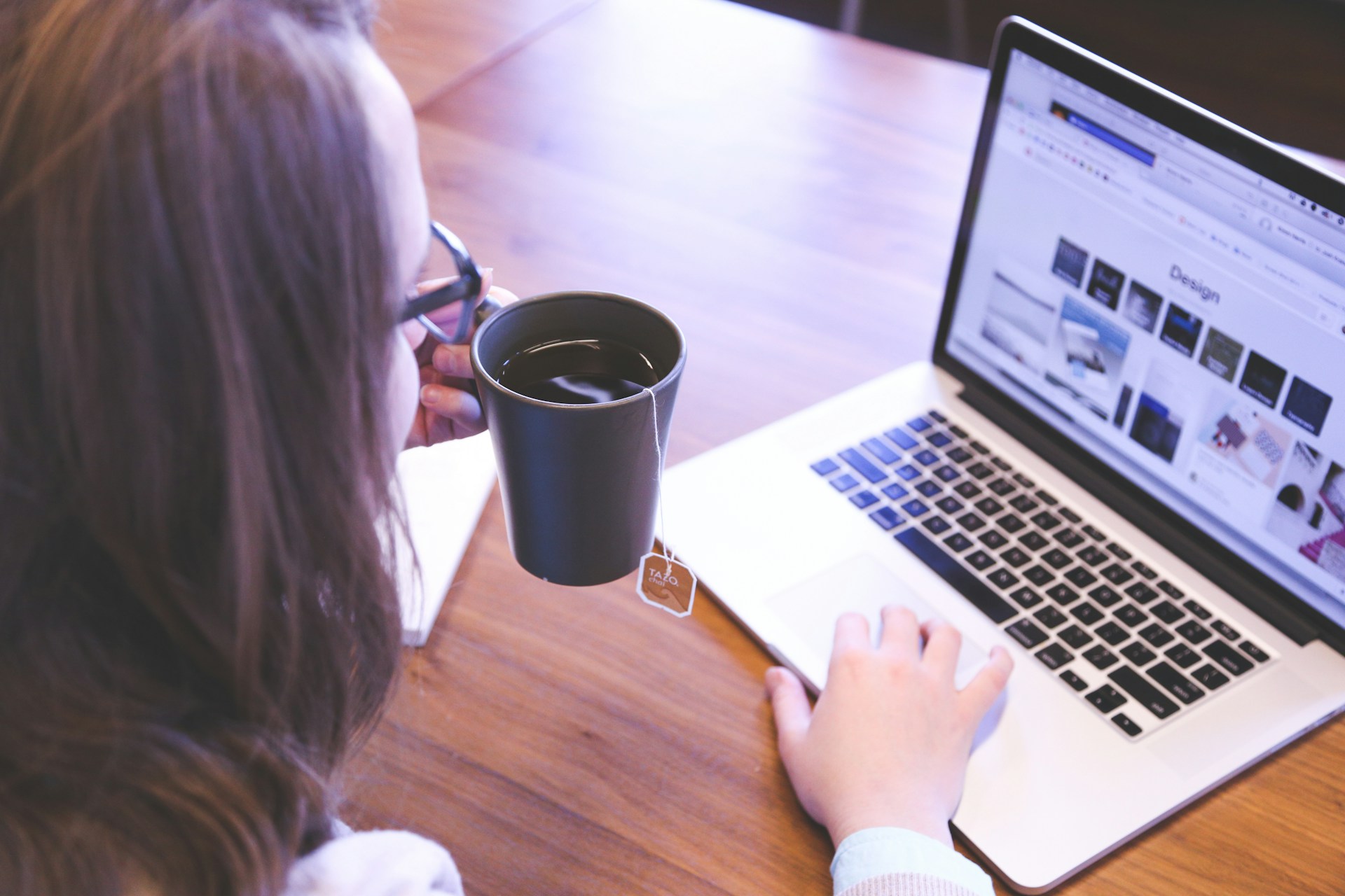 Woman holding a cup of tea in front of a laptop